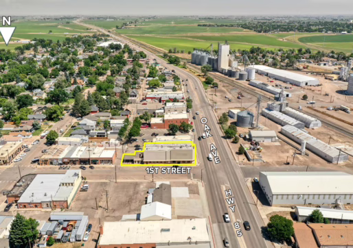 For Sale or Lease-100 Oak Ave, Eaton, CO. Aerial view of a small town with buildings, roads, and farmland. “1st Street,” “Oak Ave,” and “Hwy 85” are labeled, highlighting a Retail For Lease building outlined in yellow near their intersection. A large industrial area is on the right.