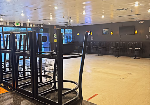 A restaurant interior with chairs stacked upside down on tables with empty floor space. The walls have some decorations and a TV.