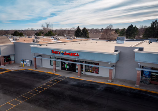 Retail For Lease-3608 W 10th St, Greeley, CO 80634-An exterior view of a strip mall with a "Party America" store at the center. The mostly empty parking lot and Retail For Lease signs hint at opportunity, while partly cloudy skies and trees frame the backdrop.