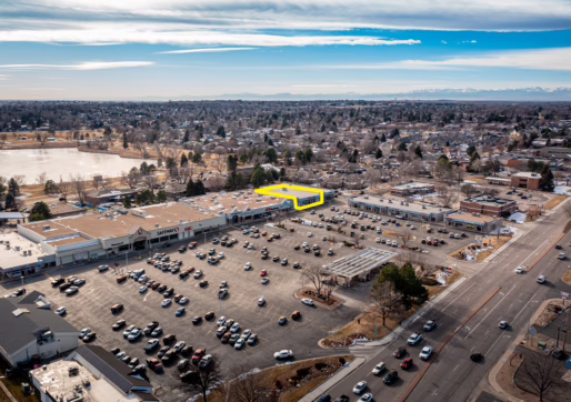 Retail For Lease-3608 W 10th St, Greeley, CO 80634-Aerial view of a large shopping center parking lot with many cars parked. One storefront outlined in yellow features Retail For Lease. Residential neighborhoods and a lake are visible in the background.