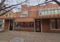 Office For Lease-809 9th St, Unit 2A, Greeley, CO 80631 - A brick building with large windows and a brown awning, bordered by leafless tree branches. The sidewalk is paved with bricks, and there is a glass door and satellite dish on the right side of the building.