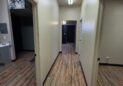 Office For Lease-809 9th St, Unit 2A, Greeley, CO 80631 - A hallway with light-colored walls and wood-patterned floors, featuring several open doorways on both sides. Fluorescent lights are on the ceiling, and rooms are visible through the doorways.