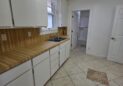 For Sale or Lease-222 Oak Ave, Eaton, CO 80615. A kitchen with white cabinets, wood-patterned countertops, a stainless steel sink, and tiled flooring. There's a window above the sink and an open doorway leading to another room with white walls.