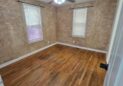 For Sale or Lease-222 Oak Ave, Eaton, CO 80615. An office with hardwood floors, two windows with white blinds, beige textured walls, and a ceiling fan with lights is shown.