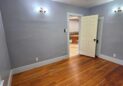For Sale or Lease-222 Oak Ave, Eaton, CO 80615. An office with light gray walls, a wooden floor, two wall sconces, a ceiling light, and an open door leading to a tiled kitchen area.