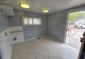 For Sale or Lease-222 Oak Ave, Eaton, CO 80615. A utility room with gray-blue walls, tiled floor, two ceiling lights, a window with sheer curtains, and an open door leading outside to a driveway with a parked car and trees visible.